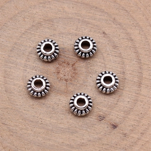 Five vintage silver alloy spacer beads with gear pattern on natural wood texture surface