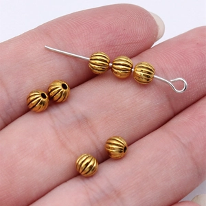 Golden pumpkin beads and silver metal pin held in hand for DIY jewelry making supplies
