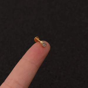 Macro shot of gold zircon labret stud with crown setting held between fingertips