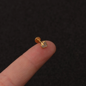 Macro detail of tiny gold heart stud with three sparkling zircons held on a fingertip