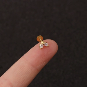 Detailed macro of gold-plated flower labret stud with white teardrop zirconia on finger