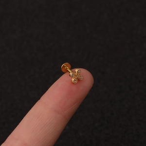 Macro shot of gold-plated clover piercing stud with zircons held on a fingertip