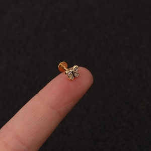 Macro shot of tiny gold butterfly labret stud with clear cubic zirconia on fingertip