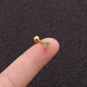 Dettaglio macro di piercing a cuore placcato in oro con zirconi tenuto tra le dita
