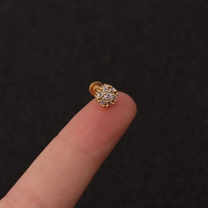 Macro shot of gold flower labret with cubic zirconia held on fingertip for scale