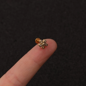 Detailed view of a small golden flower labret stud with zircons held on a fingertip