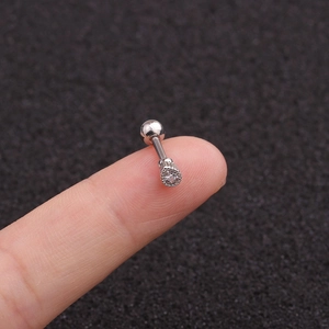 Dettaglio del micro orecchino a bottone in acciaio inossidabile con zircone tra le dita