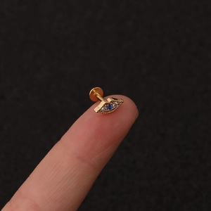 Detailed close-up of a gold Evil Eye cartilage stud with blue and white zircons on fingertip