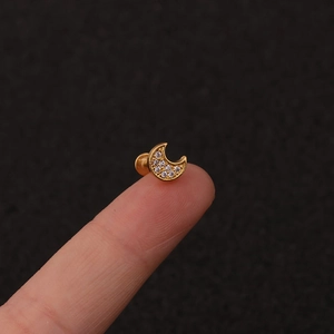 Macro shot of a tiny gold moon piercing stud with sparkling zircons held on a fingertip