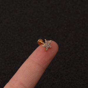 Macro shot of tiny gold star piercing stud with white zircons on a fingertip