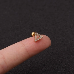 Macro di un piccolo orecchino a triangolo dorato con zirconi sulla punta di un dito