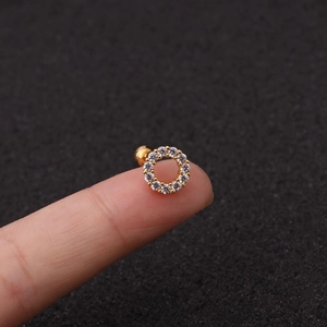Dettaglio di un piercing all'orecchio dorato con zirconi incastonati e chiusura a sfera
