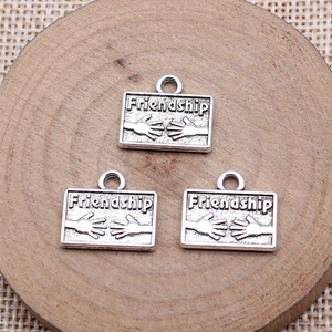 Three antique silver friendship charms for DIY jewelry making on a wooden board