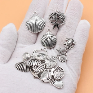 Set of 20 antique silver ocean themed sea shell and starfish alloy charms held in a gloved hand