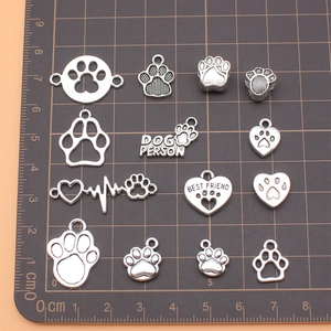 Set of 14 antique silver dog paw and heart charms for DIY jewelry making on scale mat