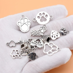 Set of 14 antique silver dog paw charms and pet heart pendants shown in hand