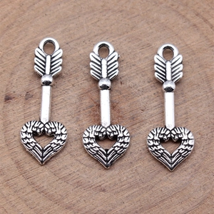 Three antique silver heart arrow charms on a wood background for DIY jewelry making