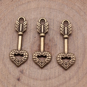 Vintage bronze heart arrow charms for DIY jewelry making on natural wood background