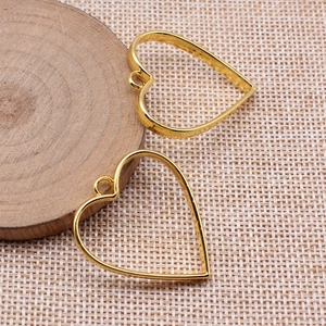 Goldene herzförmige hohle Metallrahmen-Anhänger für DIY-Schmuck auf einem Holzsockel