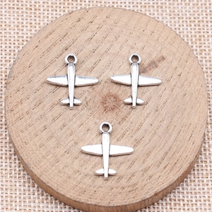 Tres colgantes de avión en plata antigua para hacer joyas DIY sobre posavasos de madera