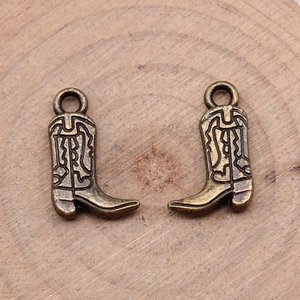 Pair of vintage bronze cowboy boot pendants with wavy textures on a wood background