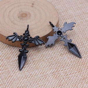Gothic black metal cross wing pendant with bat wings and spear tip on a wooden base