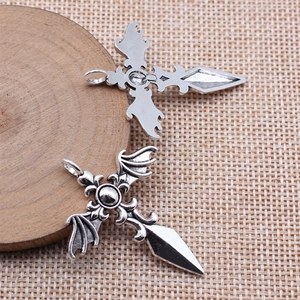 Gothic silver alloy cross pendant with bat wings and dagger design on wood base