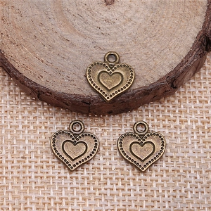 Tre ciondoli a cuore in bronzo vintage con bordi a pois su legno rustico e tessuto intrecciato