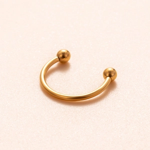 Dettaglio di un anello a ferro di cavallo dorato per naso con sfere su sfondo rosa