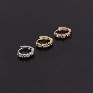 Close-up of three mini huggie earrings in silver, gold, and rose gold with pavé zircon