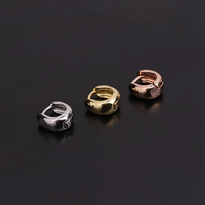 Detailed view of three polished huggie hoop earrings in silver, gold, and rose gold finishes