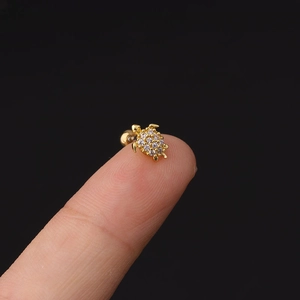 Dettaglio macro di un orecchino a forma di tartaruga dorata con zirconi su un dito