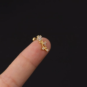 Dettaglio di un piccolo orecchino a fiore dorato con zirconi tenuto tra le dita