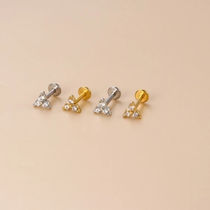 Close-up of gold and silver stainless steel labret studs with three-stone zircon triangles