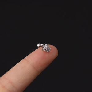 Dettaglio macro di un piccolo orecchino a tartaruga in argento con zirconi sulle dita