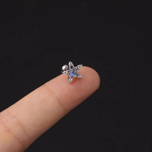 Primo piano di un piccolo orecchino a stella in acciaio con pietra blu sulla punta del dito