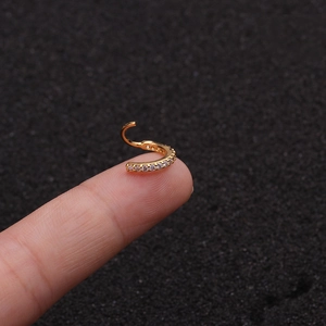 Nahaufnahme eines kleinen goldenen Nasenrings mit Zirkonia-Steinen auf einer Fingerspitze