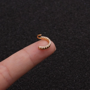 Close-up of a tiny gold nose ring with pave-set zircons held by fingers for size