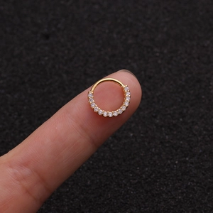 Makroaufnahme eines kleinen goldenen Nasenrings mit Zirkonia-Steinen auf einer Fingerspitze