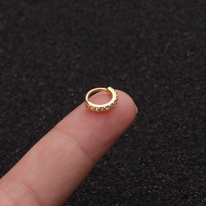 Makroaufnahme eines kleinen goldenen Nasenrings mit Zirkonia auf einer Fingerspitze