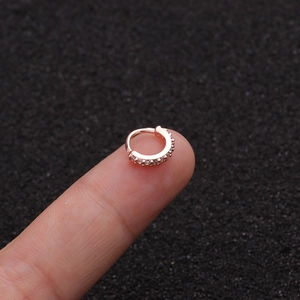 Makroaufnahme eines roségoldenen Nasenrings mit weißen Zirkonia auf einer Fingerspitze