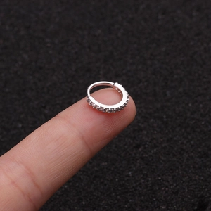 Makroaufnahme eines silbernen Nasenrings mit Zirkonia-Steinen gehalten an den Fingern