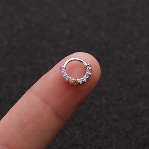 Nahaufnahme eines winzigen silbernen Nasenrings mit bunten Zirkonias auf einer Fingerspitze