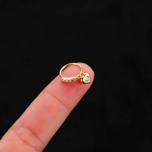 Detalle de un piercing de nariz con corazón dorado y circonitas en la punta del dedo