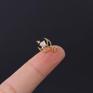 Detailaufnahme eines goldenen Mond-Pfeil-Piercings mit Opal-Herz auf einer Fingerspitze