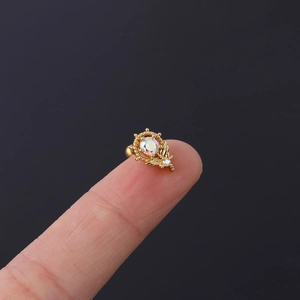 Makroaufnahme eines goldenen Steuerrad-Ohrrings mit irisierendem Kristall auf Finger