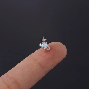 Makroaufnahme eines kleinen silbernen Kreuz-Ohrsteckers mit Zirkonia auf einer Fingerspitze
