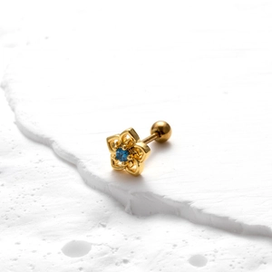 Détail de la boucle d'oreille fleur dorée avec pierre bleue sur pierre texturée