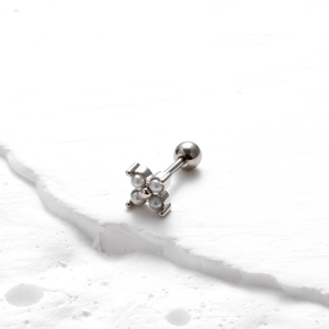 Détail macro d'un piercing en acier argenté avec quatre perles sur socle en pierre