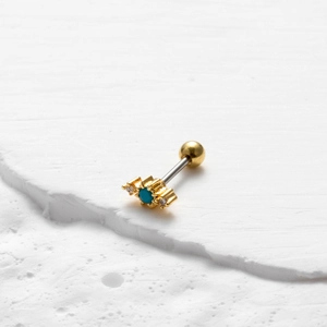 Detailopname van gouden kraakbeenoorpiercing met blauwe steen en kristallen op stenen tray
